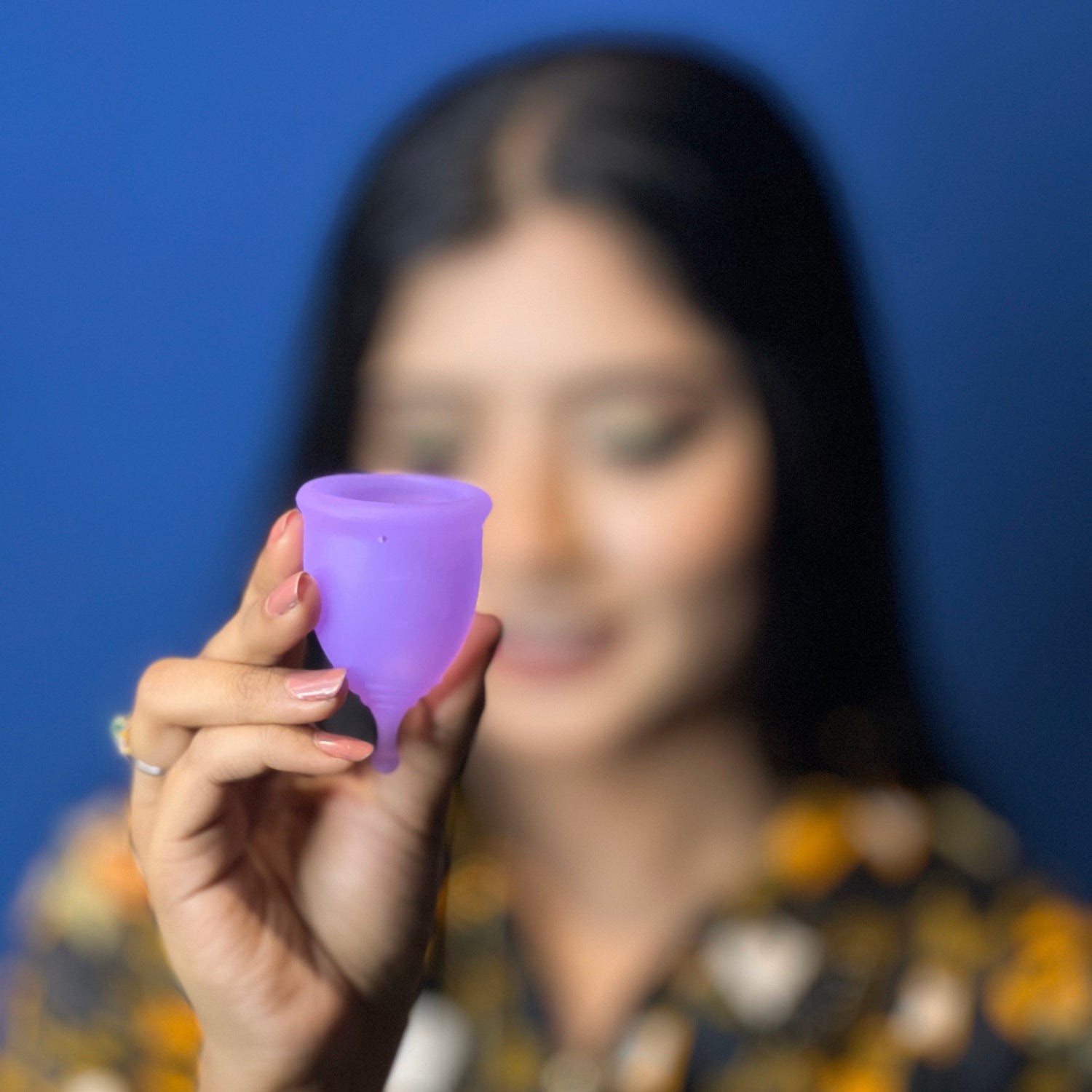 Person holding a purple menstrual cup against a blue background