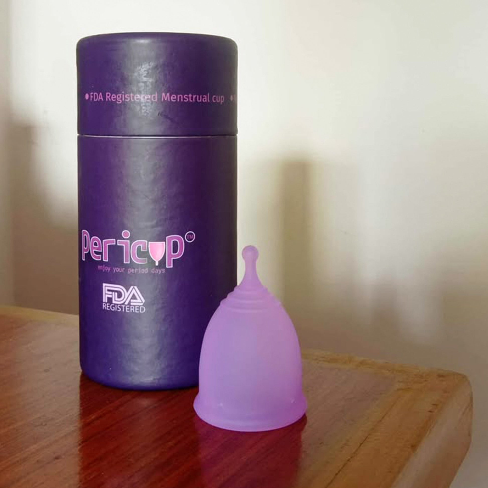 Purple menstrual cup and its packaging on a wooden surface with a plain background
pericup-fda-registered-menstrual-cup-bangladesh